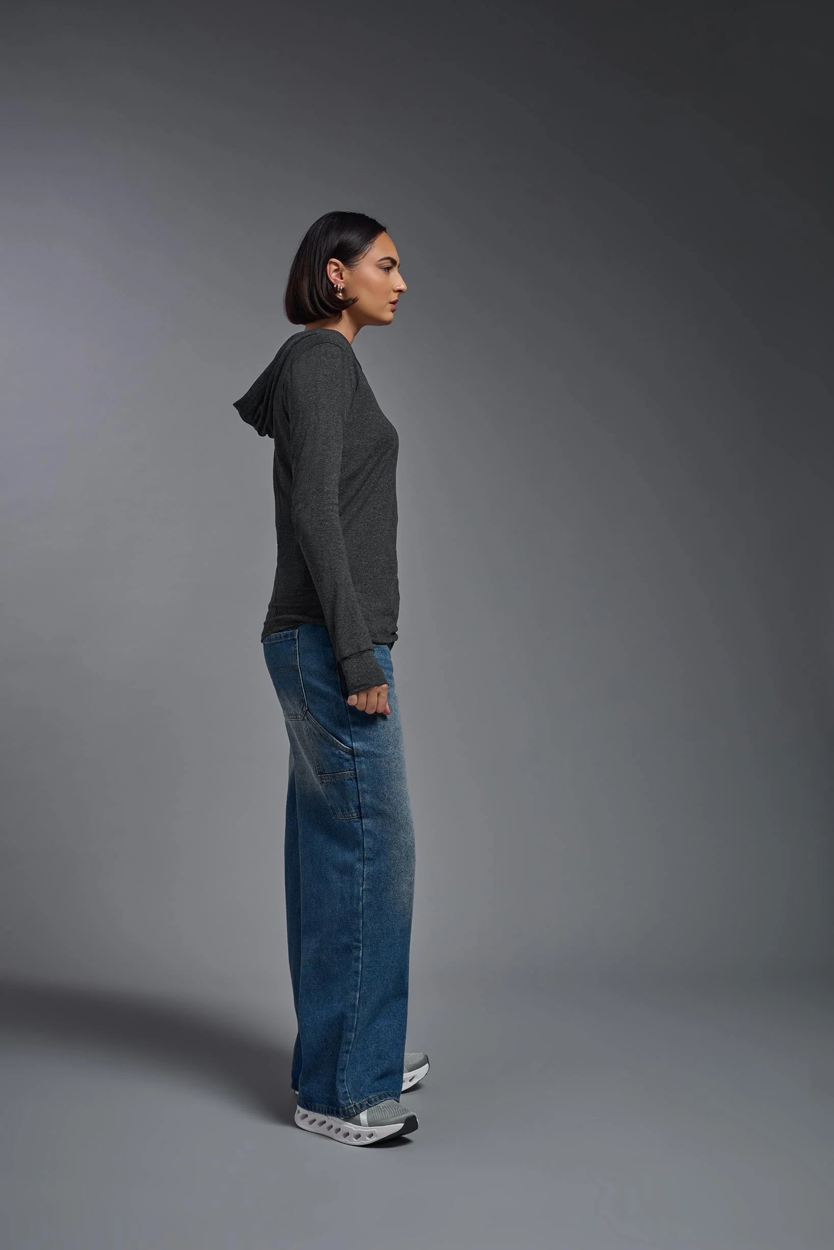 Person wearing a dark gray long-sleeve shirt and blue jeans standing against a gray background