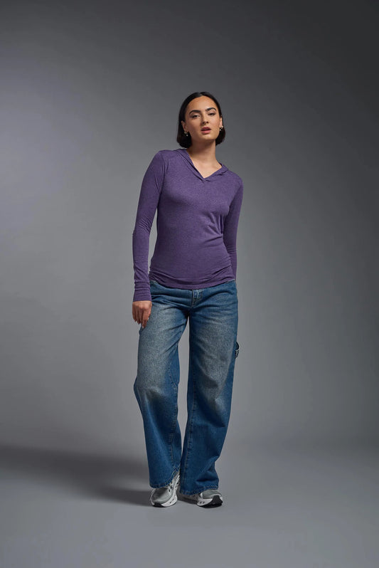 Woman wearing a purple long-sleeve shirt and blue jeans against a gray background