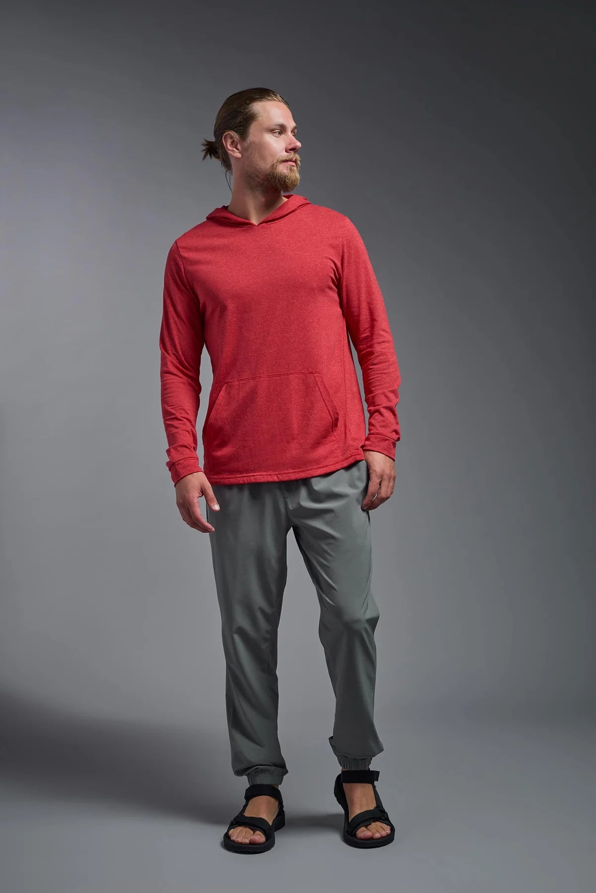 Man wearing a red hoodie and gray pants standing against a gray background
