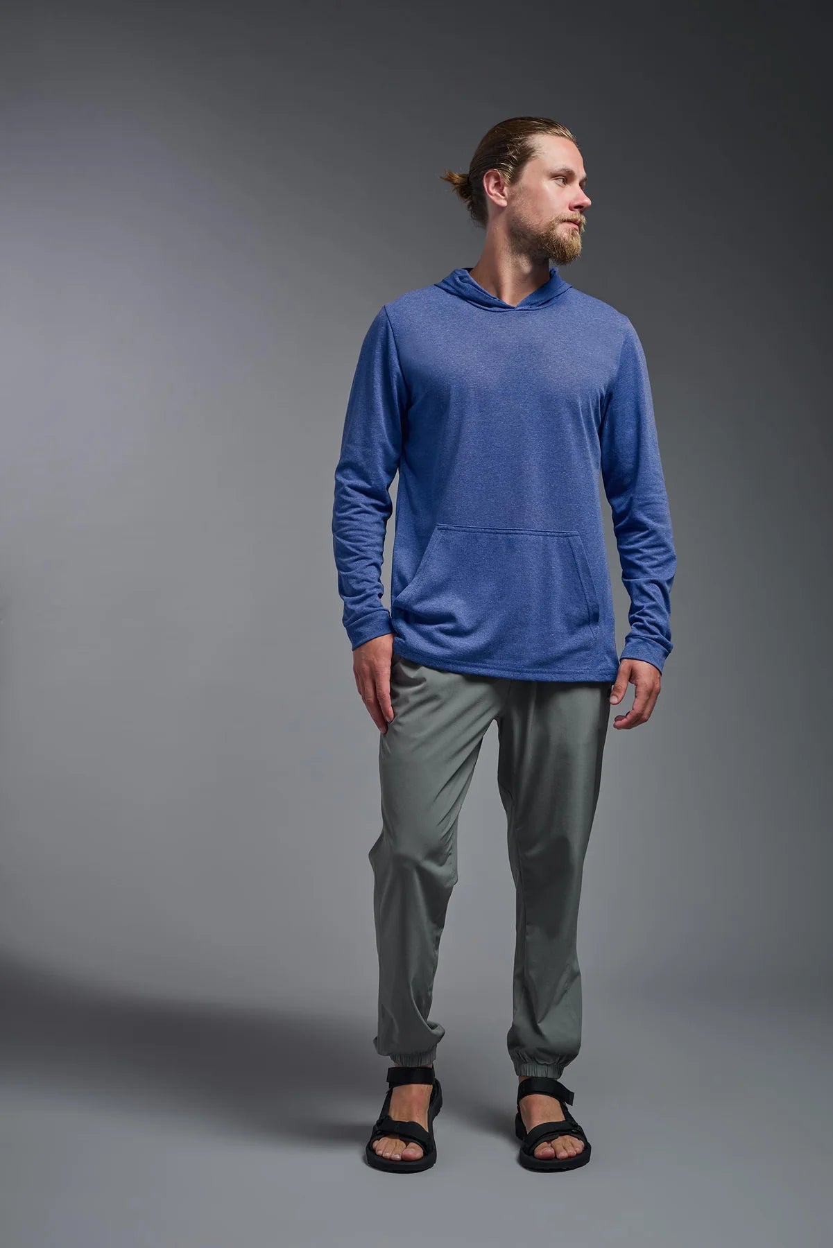 Man wearing a blue hoodie and gray pants on a gray background