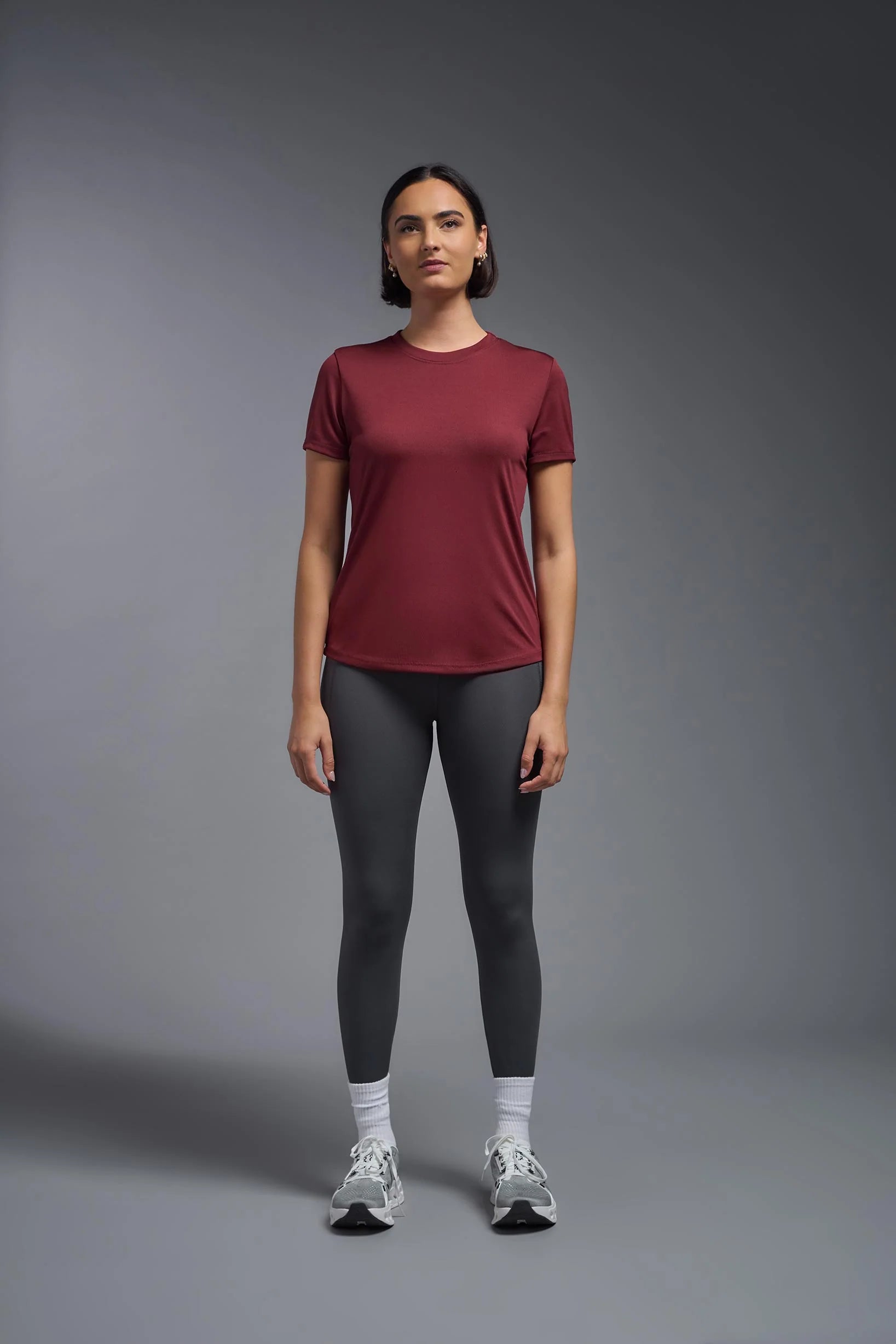 Woman wearing a maroon t-shirt and black leggings on a gray background