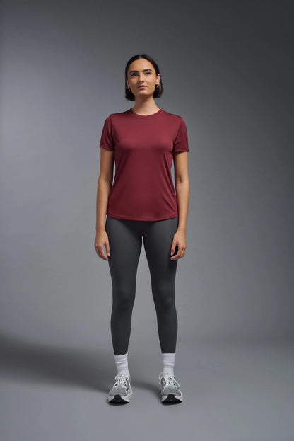Woman wearing a maroon t-shirt and black leggings on a gray background