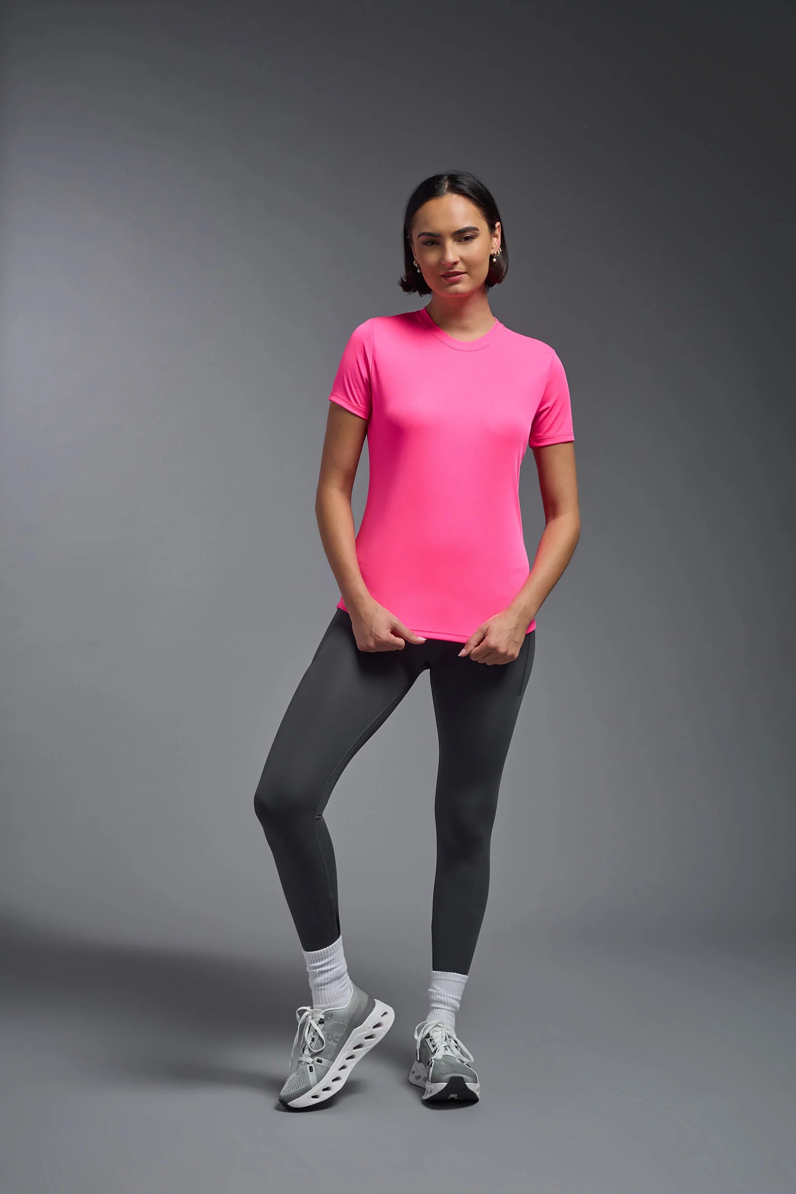 Woman wearing a bright pink athletic shirt and black leggings on a gray background