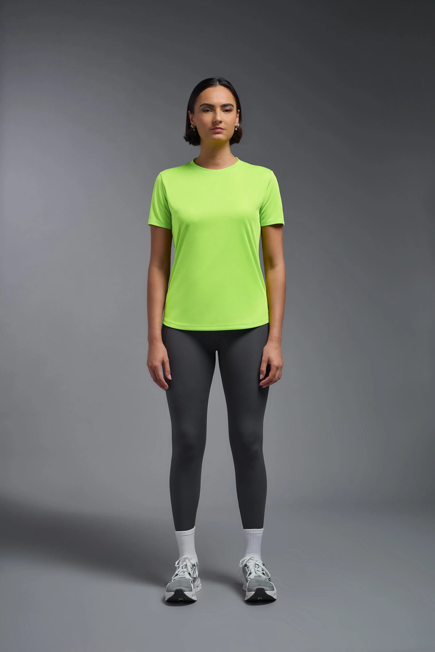 Person wearing a bright green t-shirt and gray leggings on a gray background
