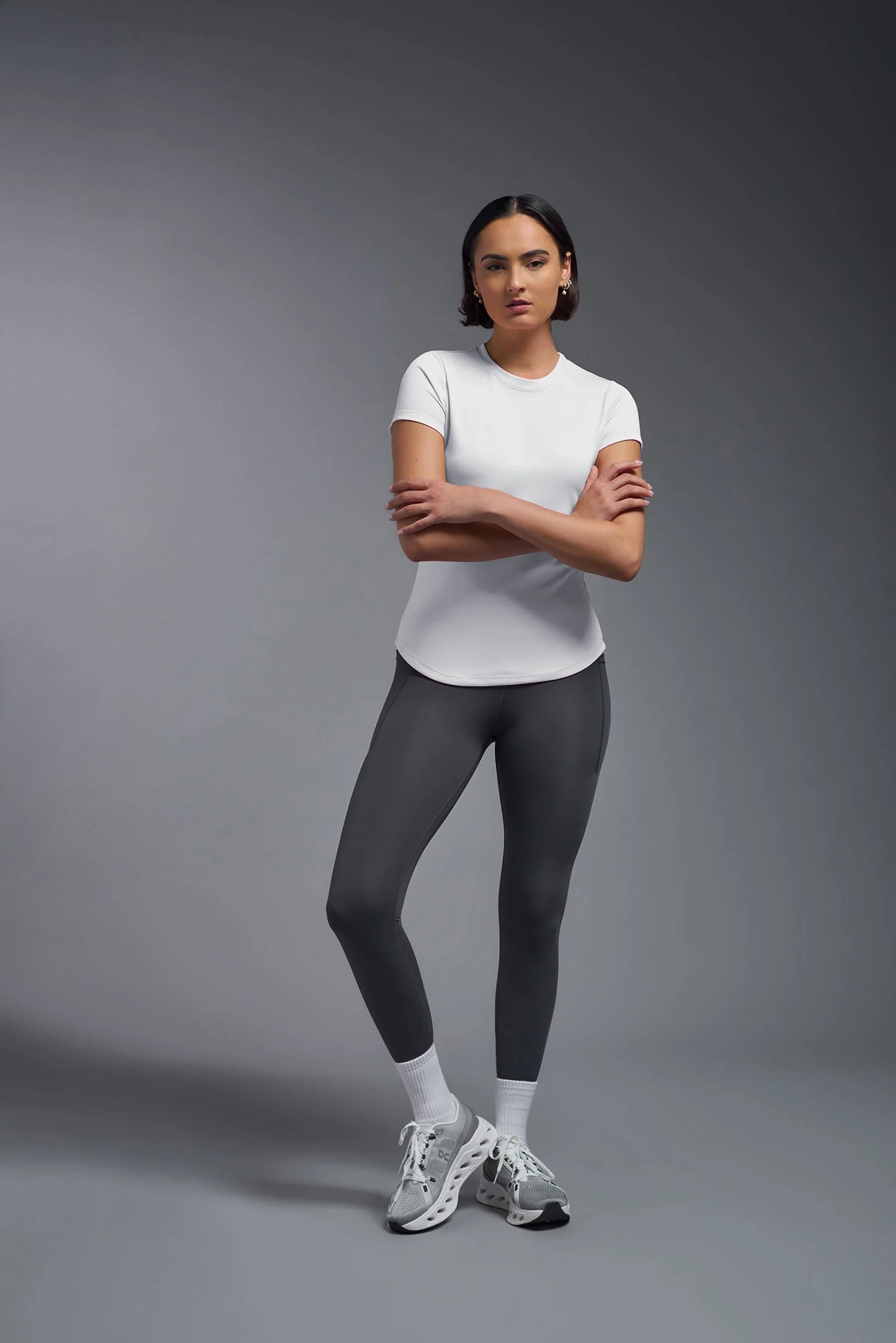 Woman wearing a white t-shirt and dark gray leggings on a gray background