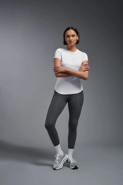 Woman wearing a white t-shirt and dark gray leggings on a gray background