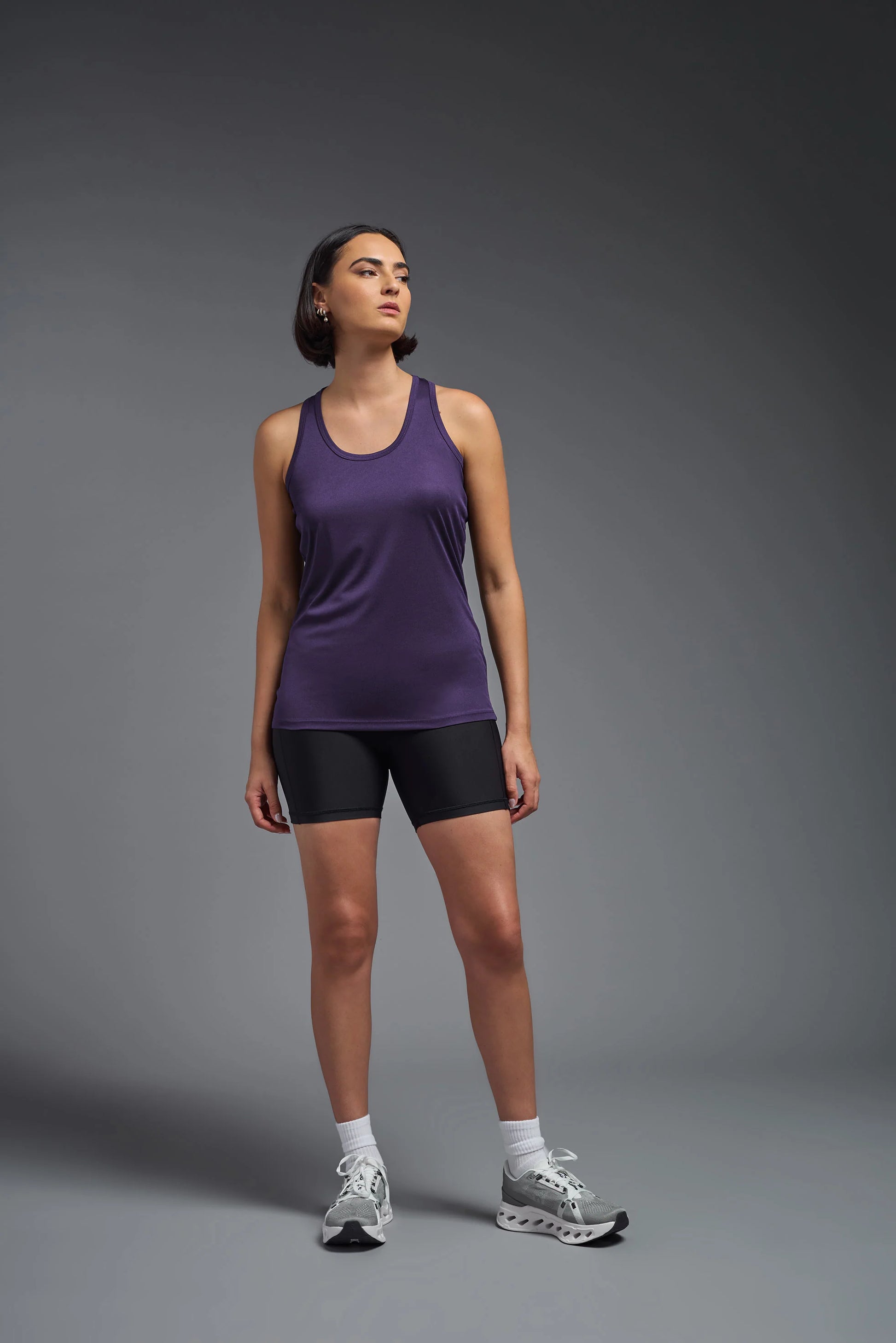Woman wearing a purple tank top and black shorts on a gray background