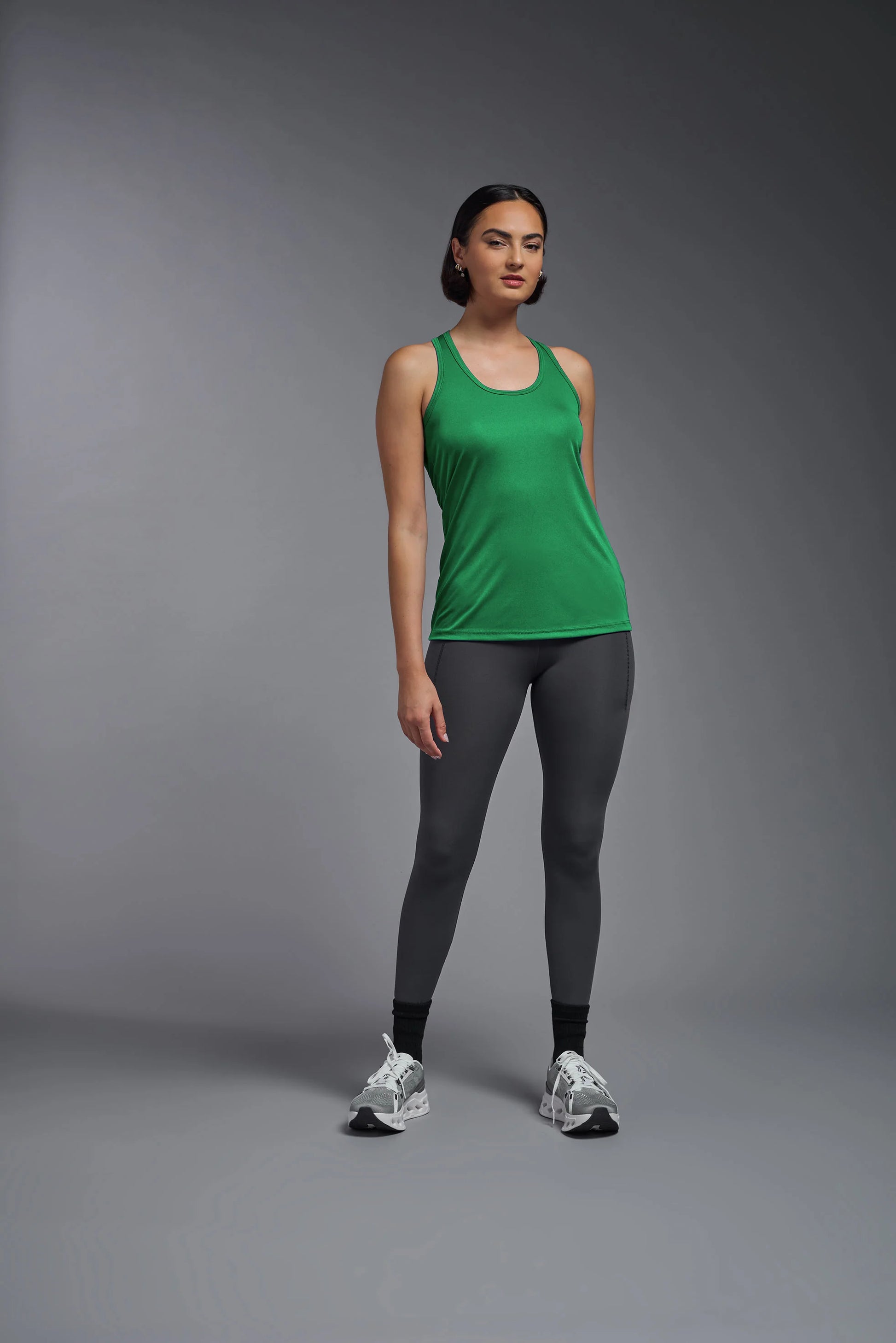 Woman wearing a green tank top and gray leggings on a gray background