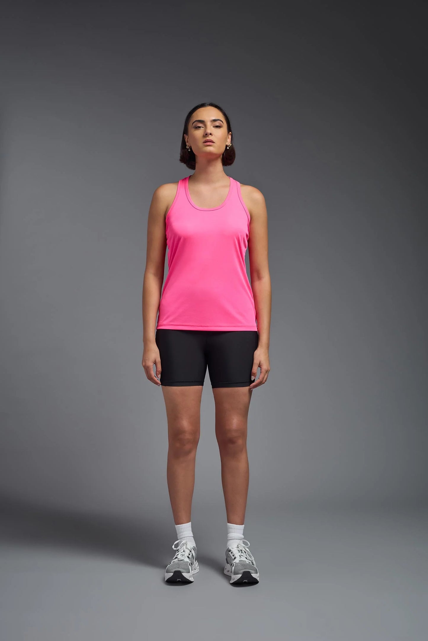 Woman wearing a pink tank top and black shorts on a gray background