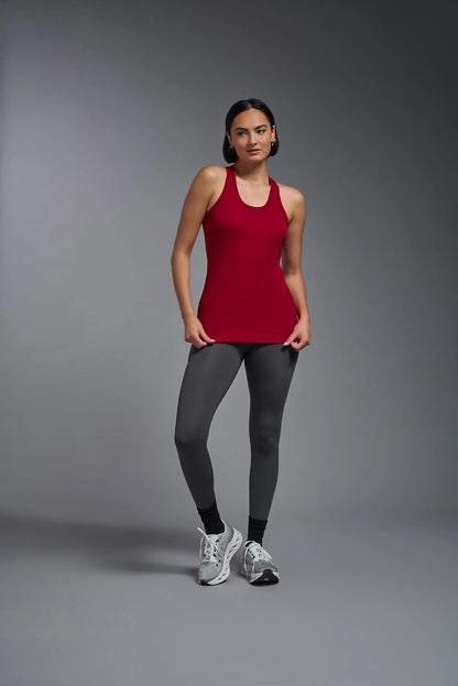 Woman wearing a red tank top and gray leggings on a gray background