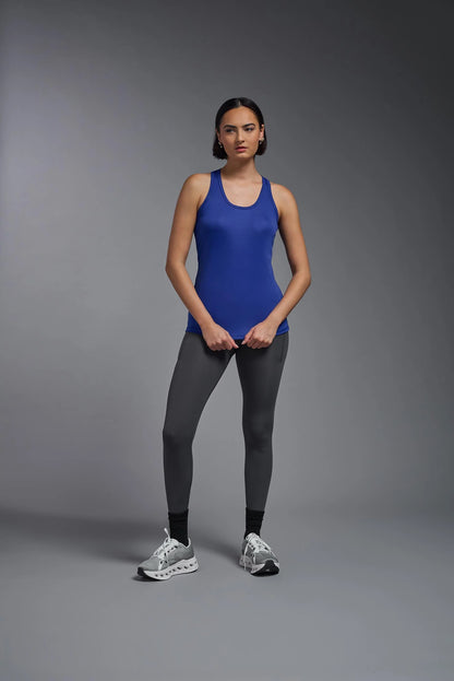 Woman wearing a blue tank top and black leggings on a gray background