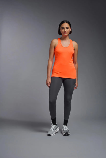 Woman wearing an orange tank top and gray leggings on a gray background