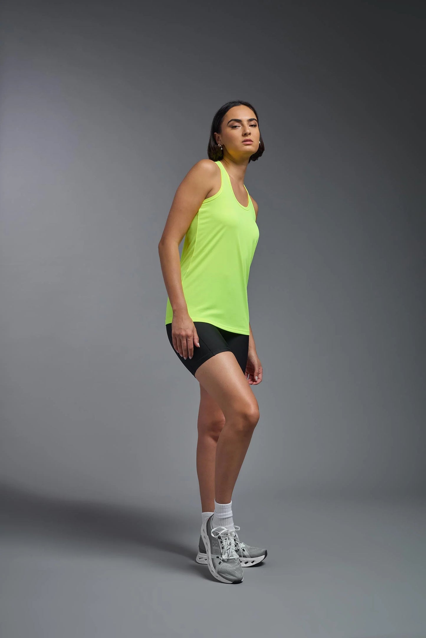 Person wearing a bright green tank top and black shorts on a gray background