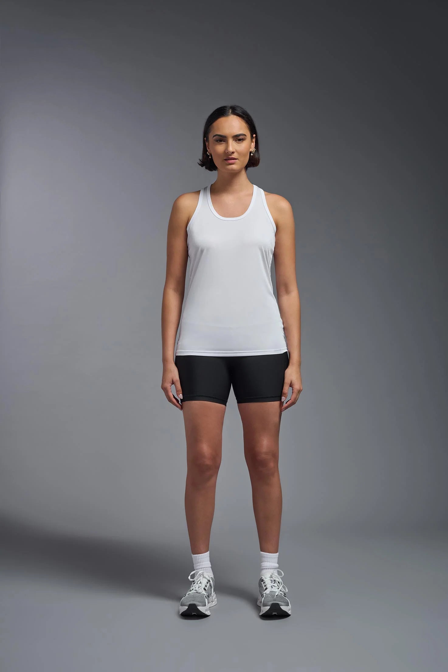 Woman wearing a white tank top and black shorts on a gray background