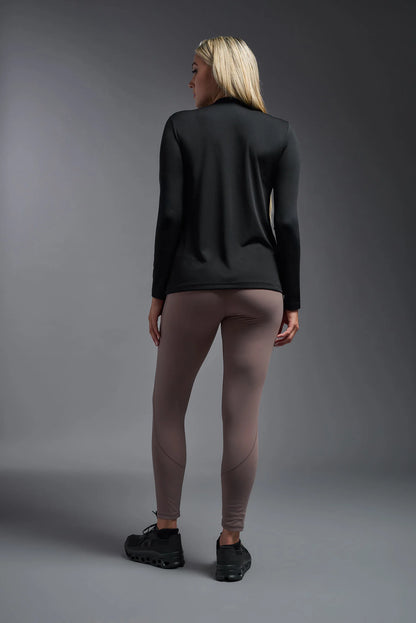 Person wearing a black long-sleeve top and beige leggings on a gray background