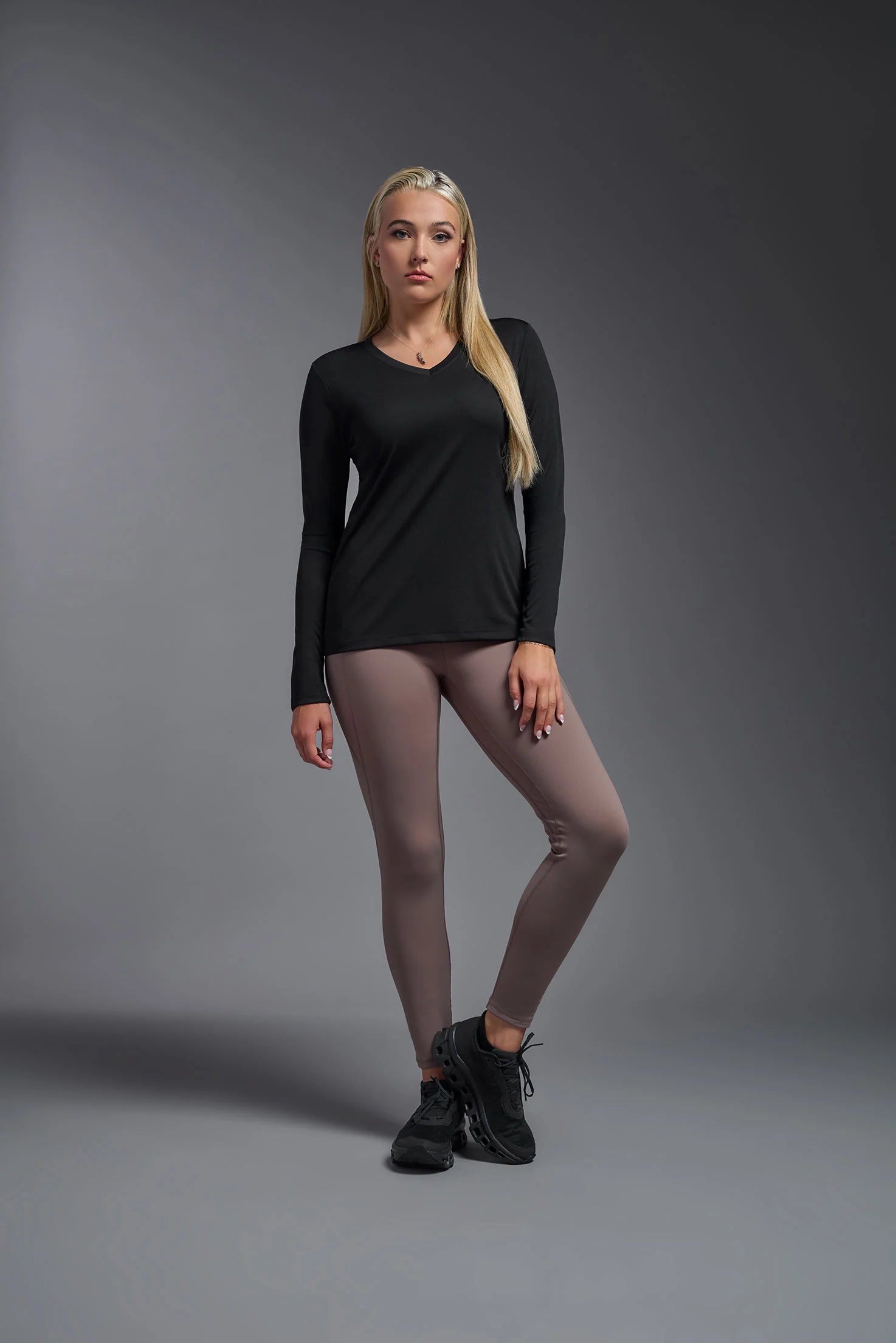 Woman wearing a black long-sleeve top and gray leggings on a gray background