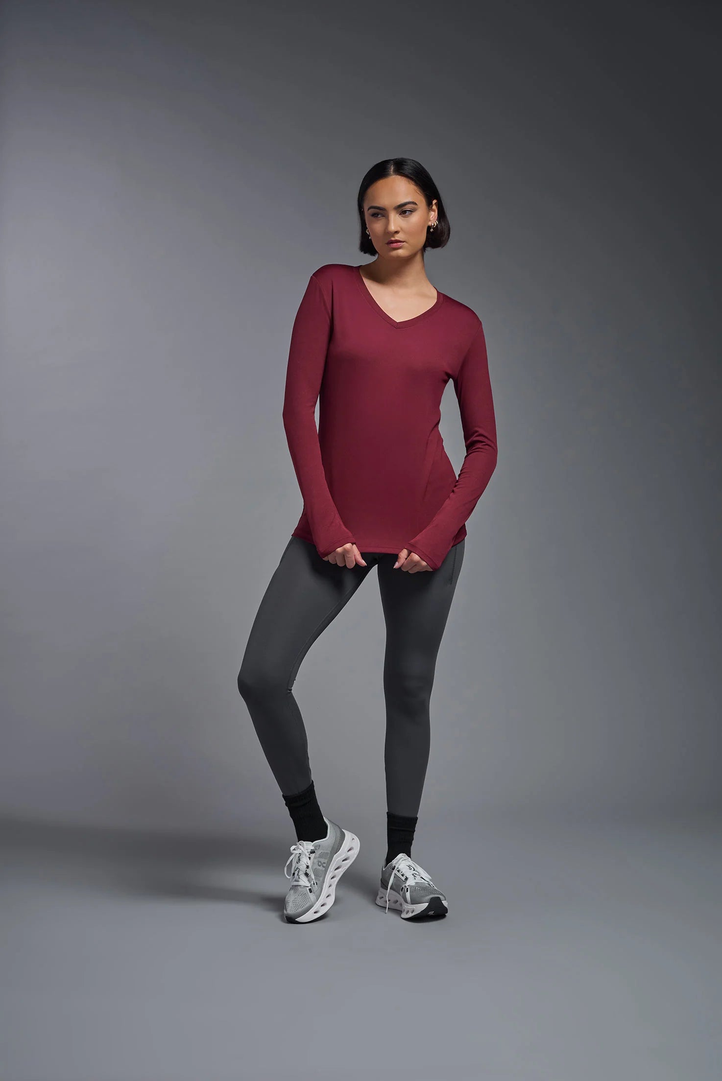 Woman wearing a red long-sleeve top and gray leggings on a gray background