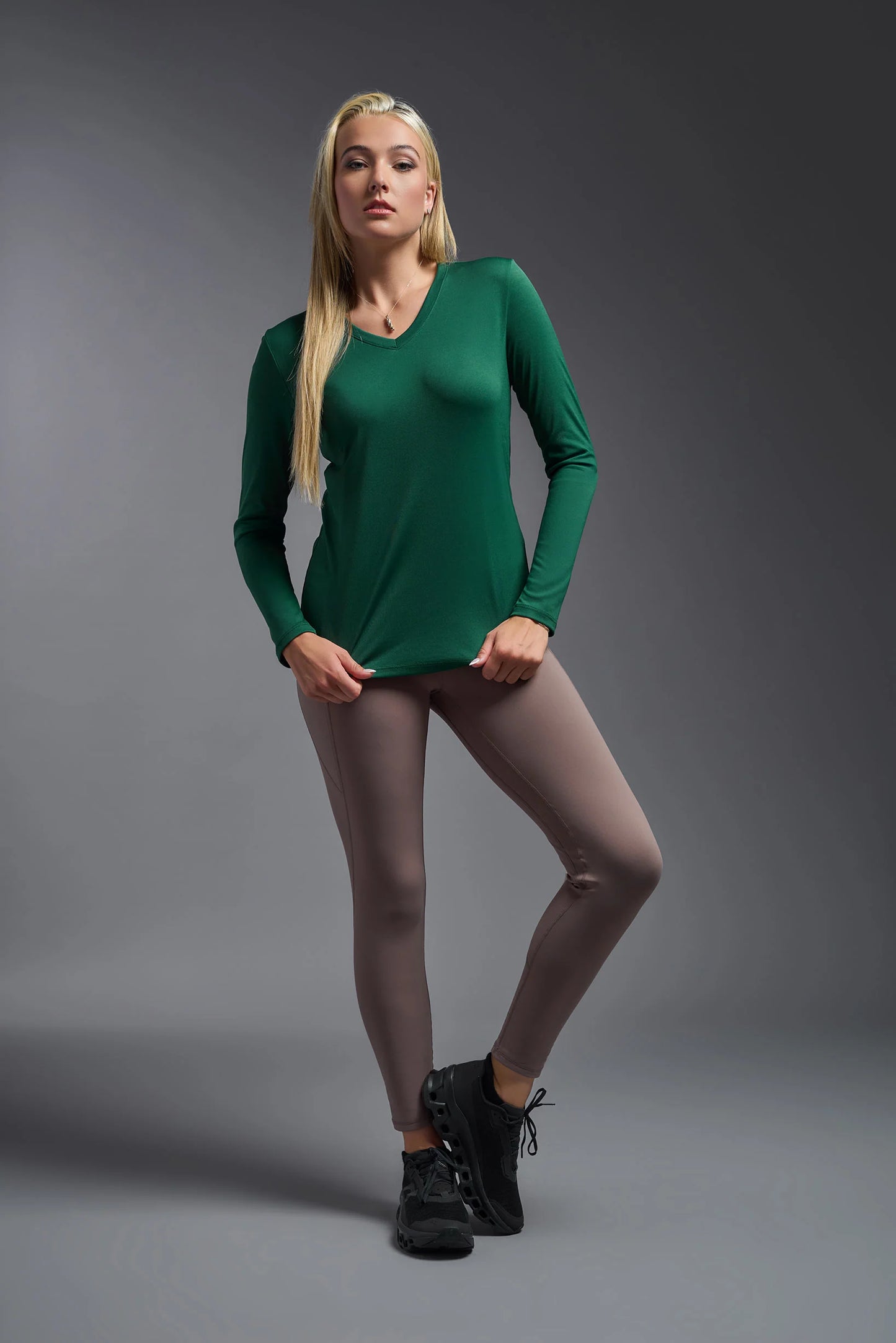 Woman wearing a green long-sleeve top and black shoes on a gray background