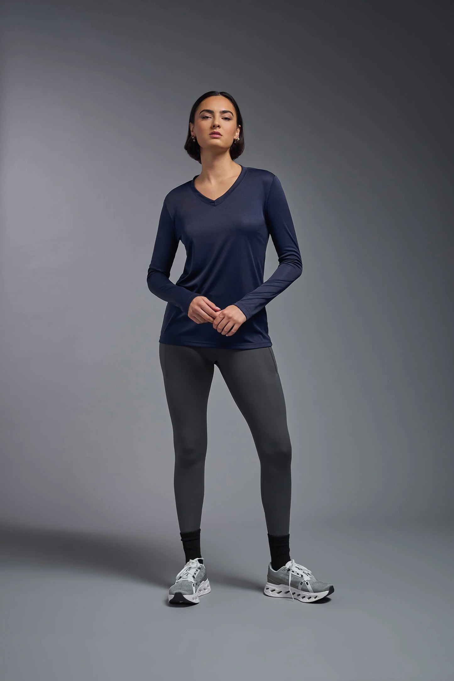 Woman wearing a navy long-sleeve top and gray leggings on a gray background