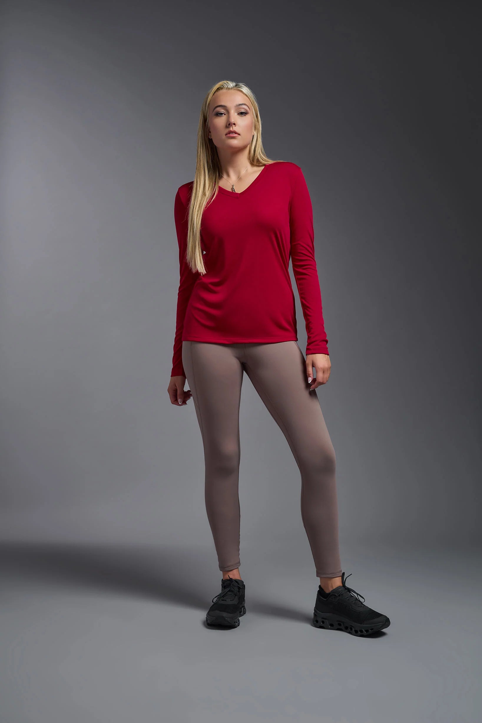 Woman wearing a red long-sleeve top and beige leggings on a gray background