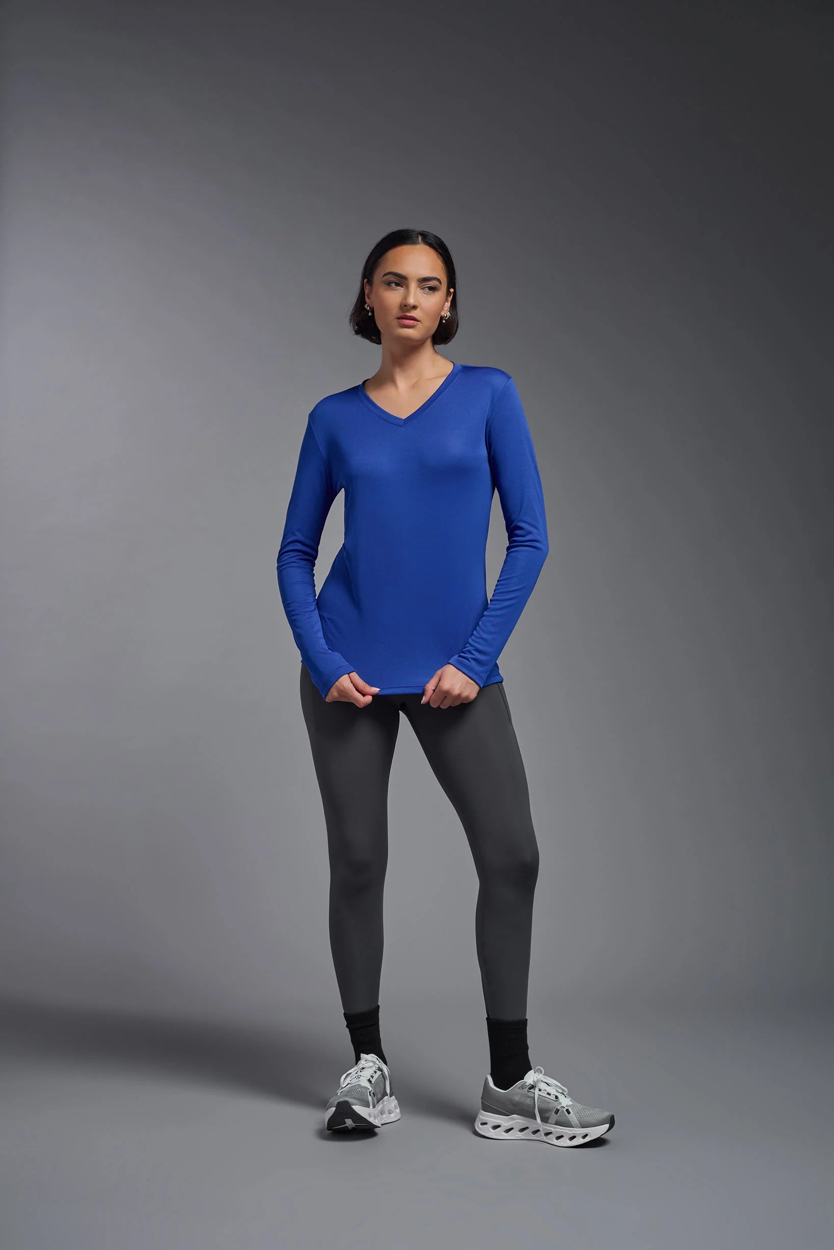 Woman wearing a blue long-sleeve top and gray leggings on a gray background