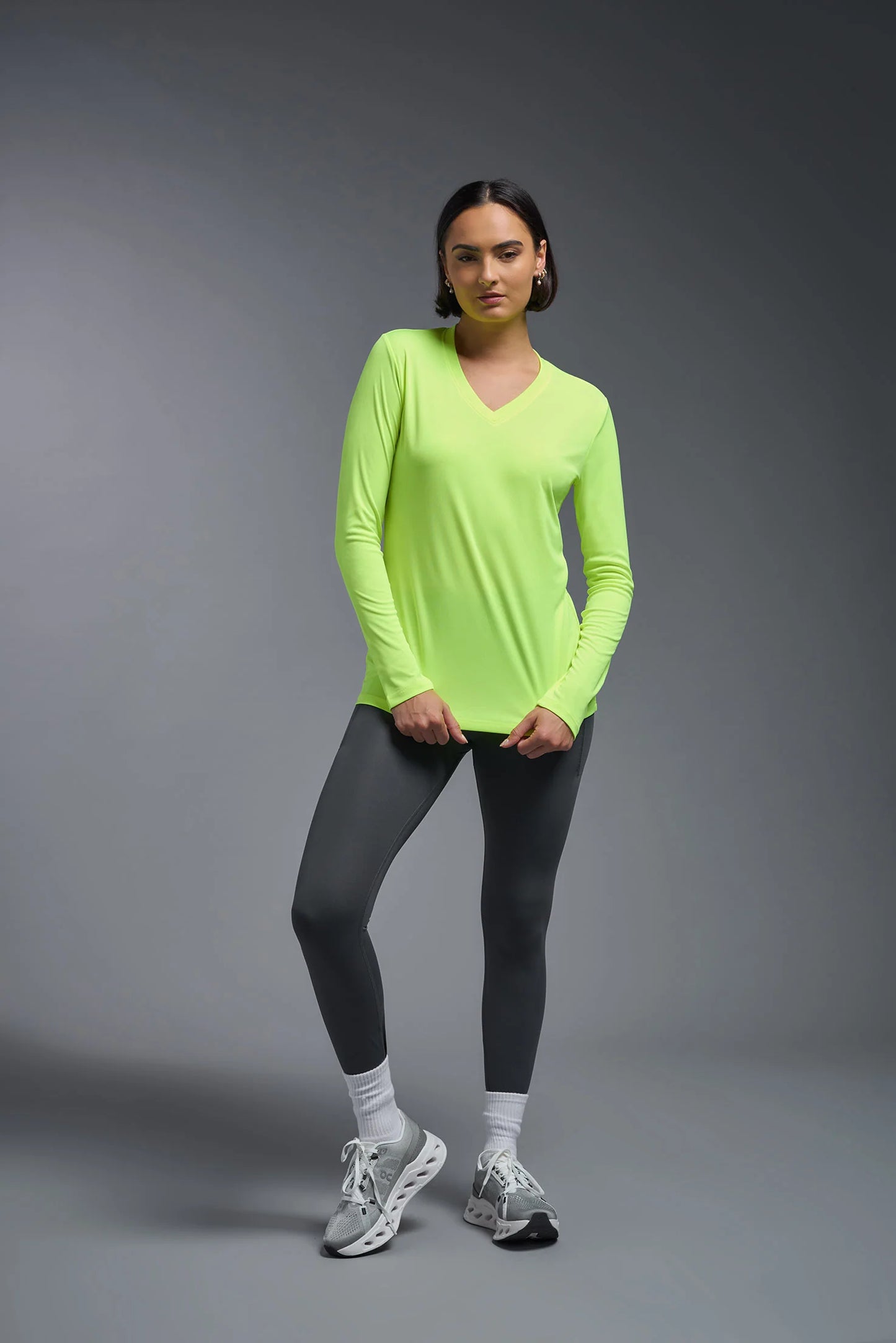 Person wearing a bright green long-sleeve top and black leggings on a gray background