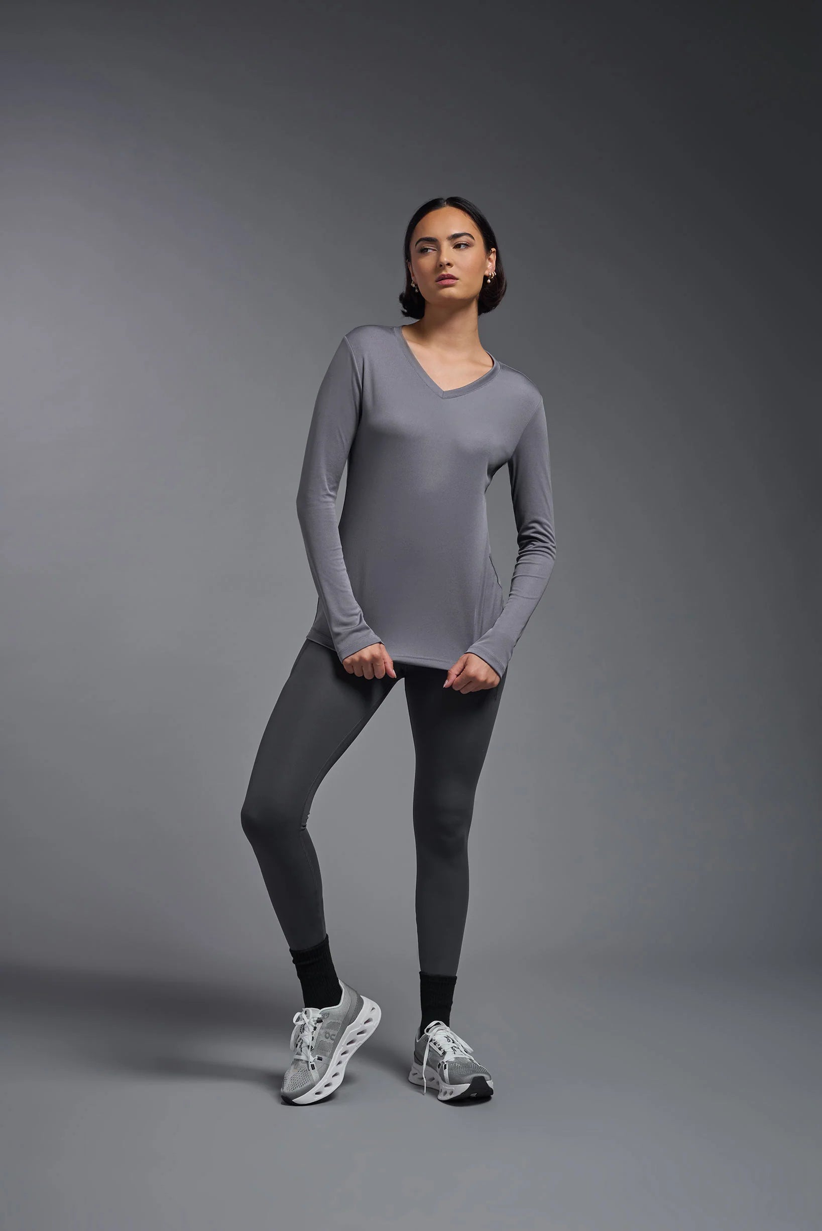 Woman wearing a gray long-sleeve top and leggings on a gray background