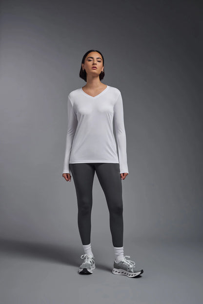 Woman wearing a white long-sleeve top and gray leggings on a gray background