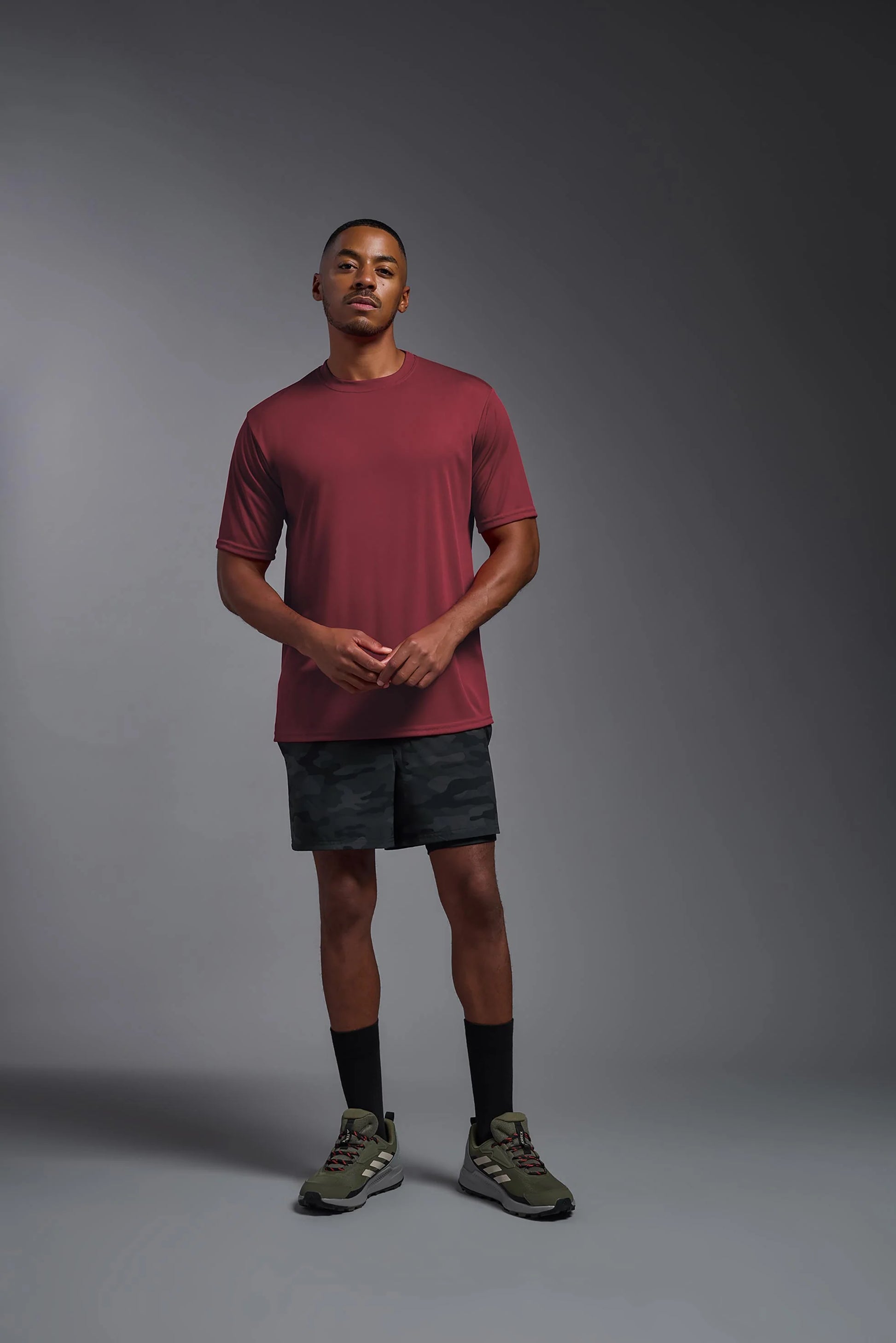 Man wearing a maroon t-shirt and black shorts on a gray background
