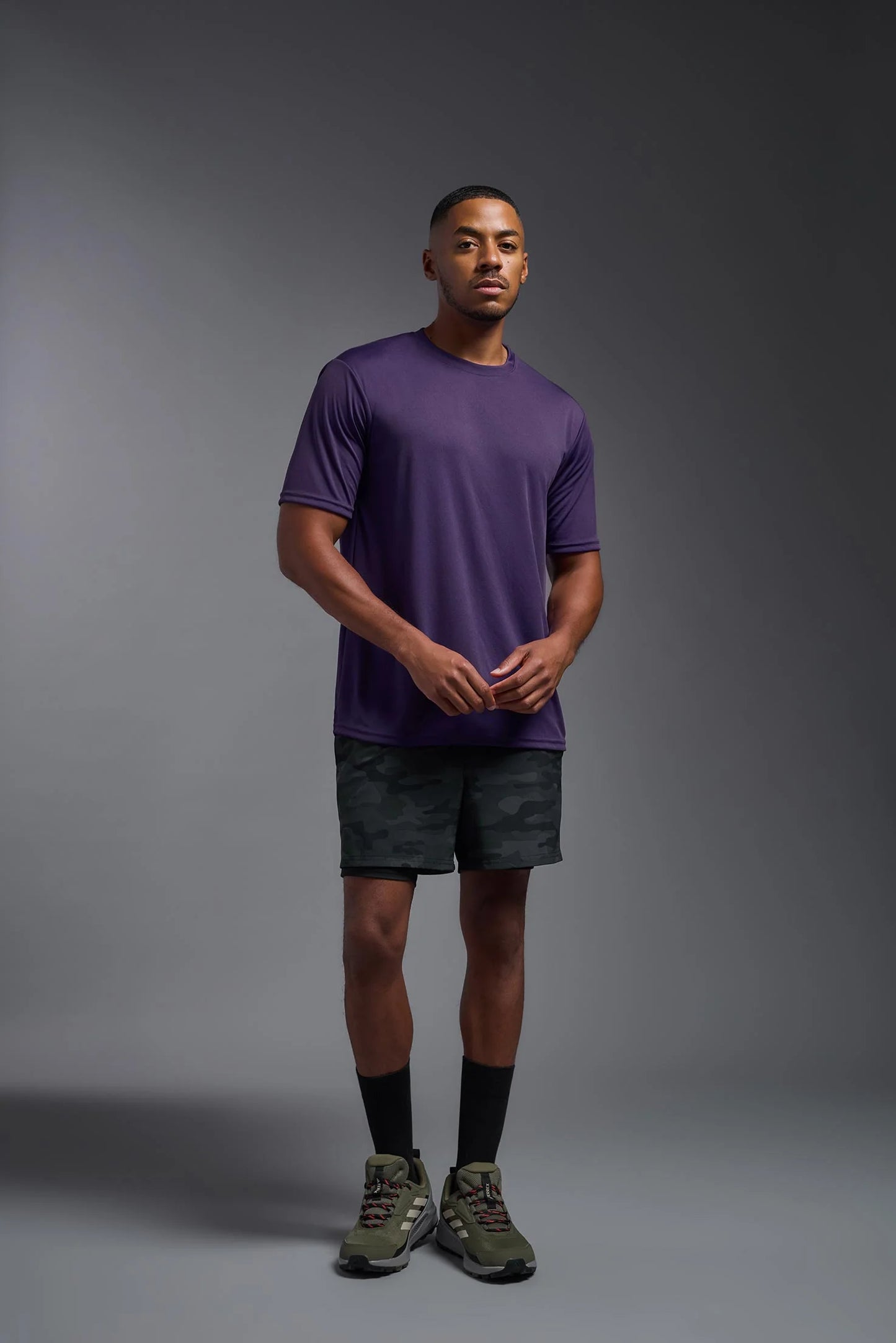 Man wearing a purple t-shirt and black shorts on a gray background