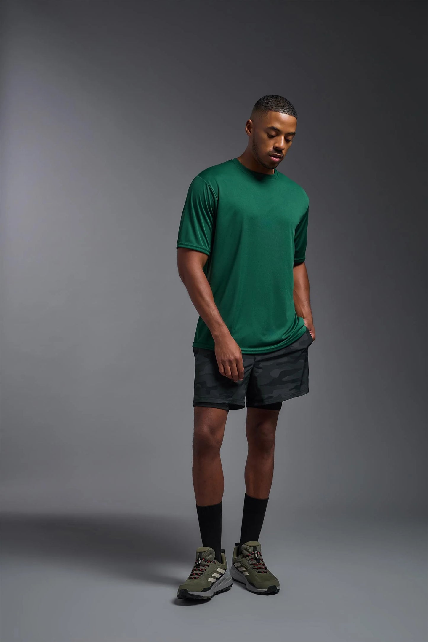 Man wearing a green t-shirt and gray shorts on a gray background