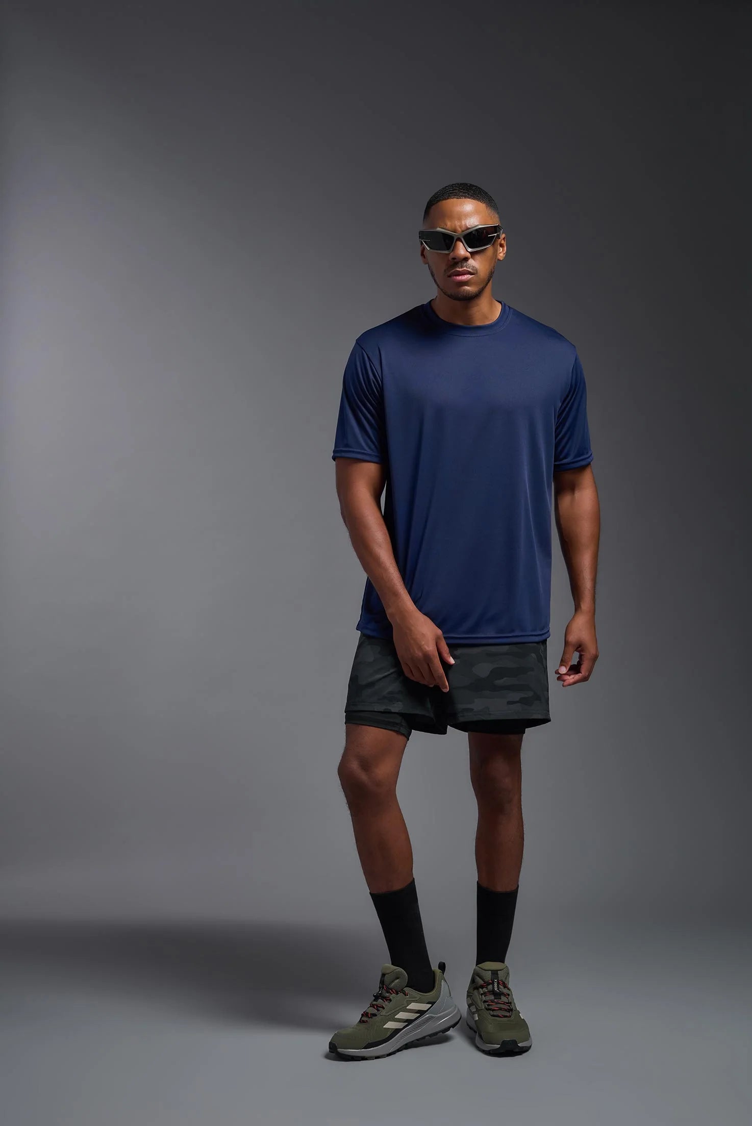 Man wearing a blue athletic shirt and dark shorts on a gray background