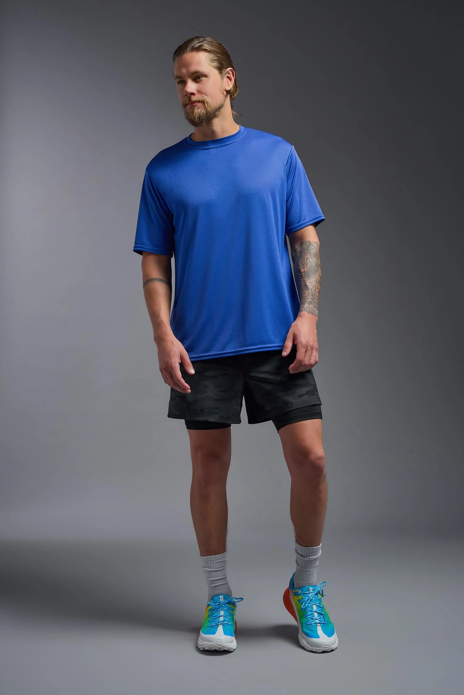 Man wearing a blue t-shirt, black shorts, and blue sneakers on a gray background