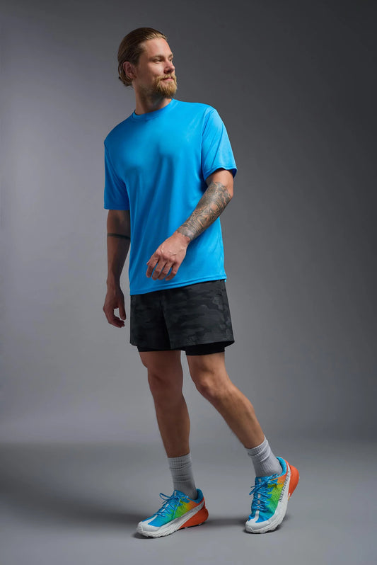 Man wearing a blue t-shirt, black shorts, and colorful sneakers on a gray background