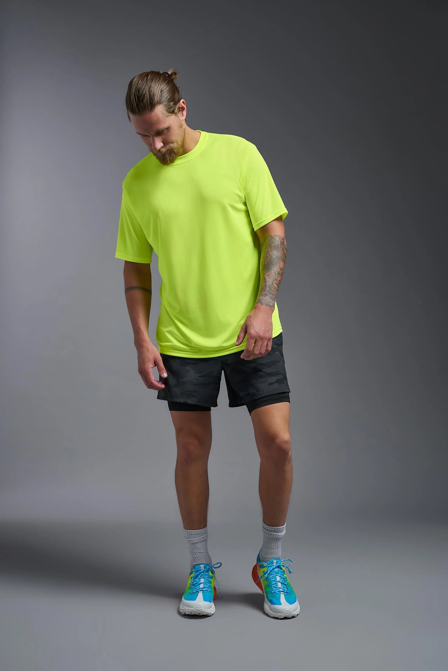 Man wearing a bright green shirt, black shorts, and blue sneakers on a gray background