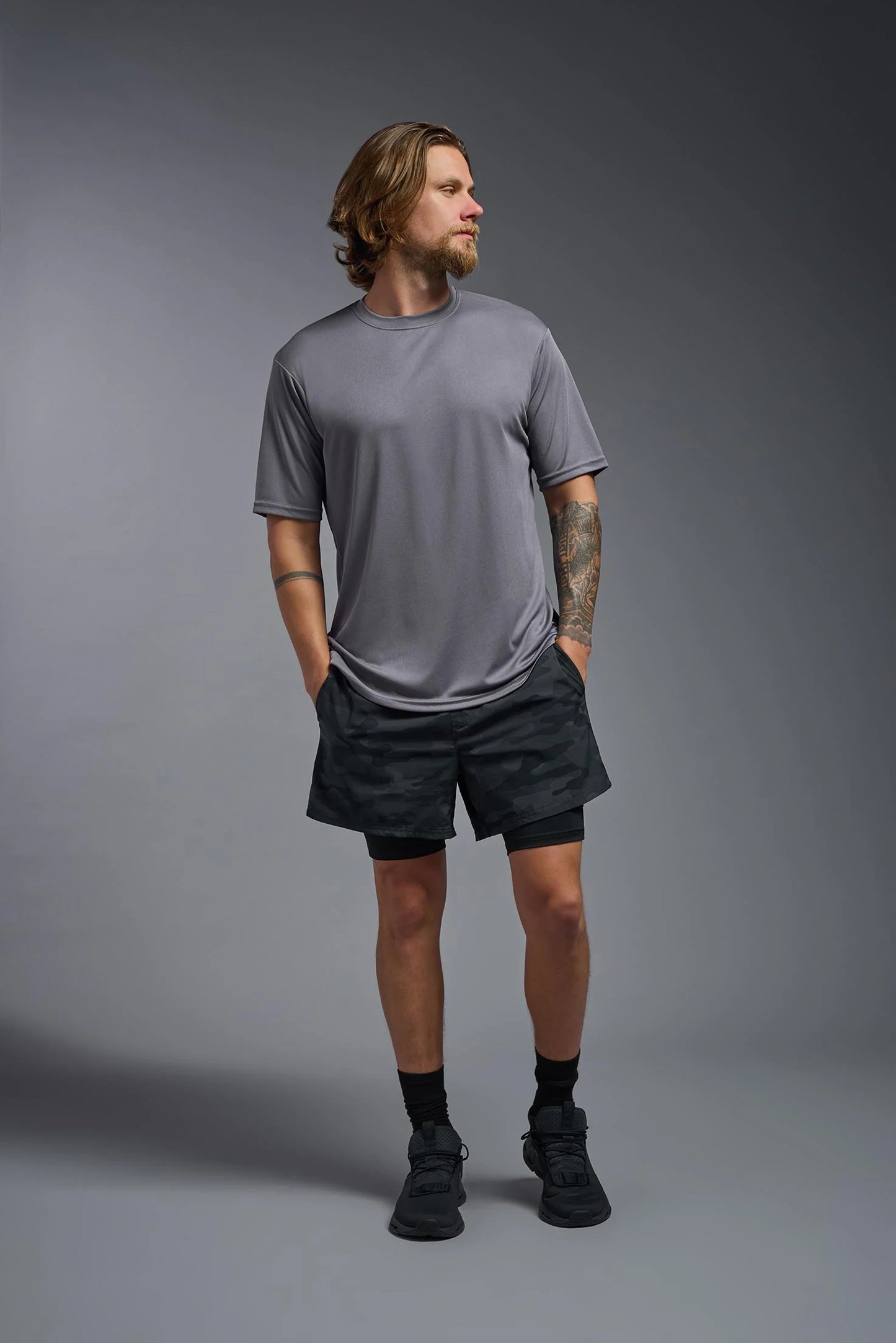 Man wearing a gray t-shirt and black shorts standing against a gray background