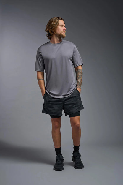 Man wearing a gray t-shirt and black shorts standing against a gray background
