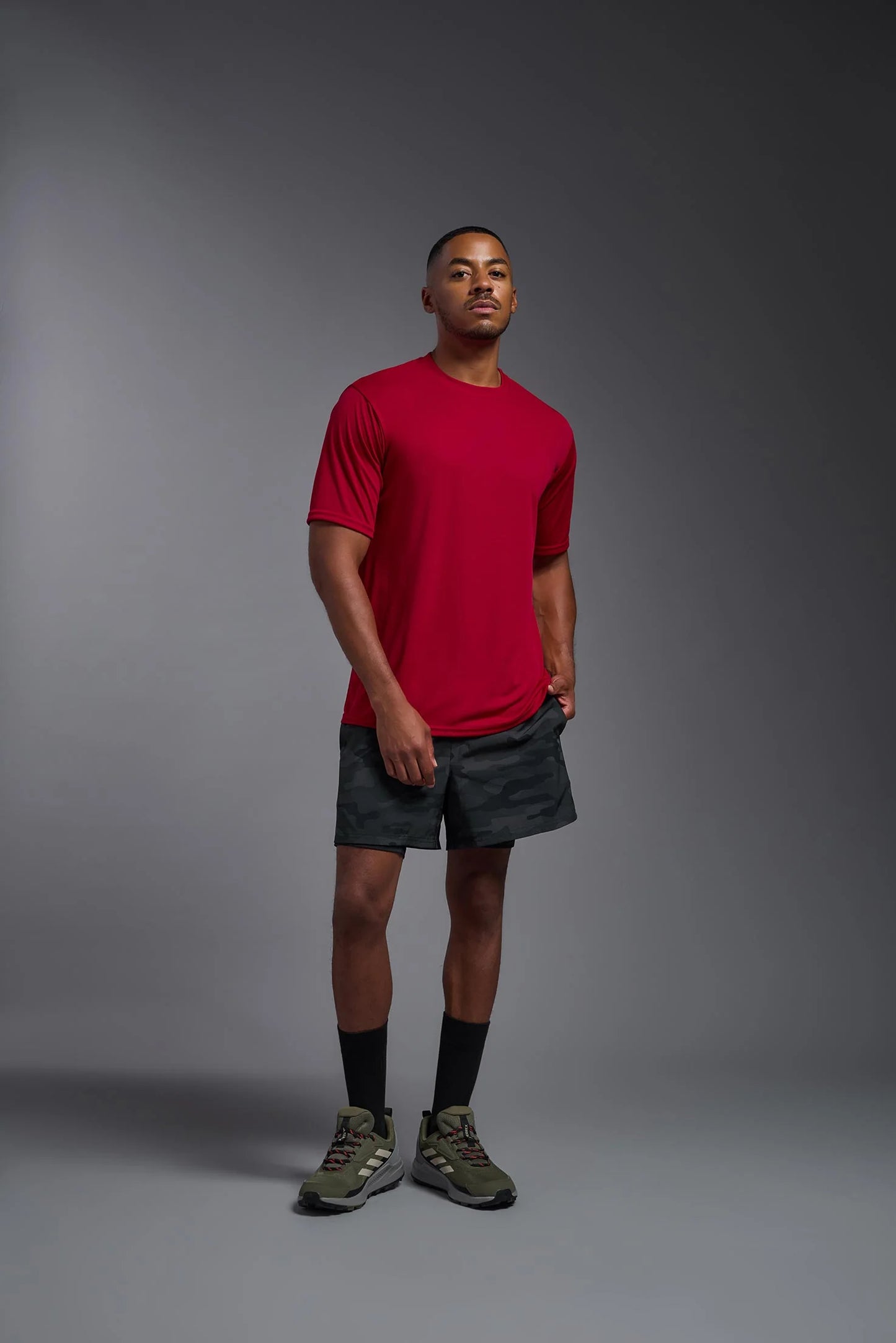 Man wearing a red t-shirt and black shorts standing against a gray background