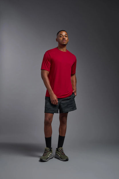 Man wearing a red t-shirt and black shorts standing against a gray background