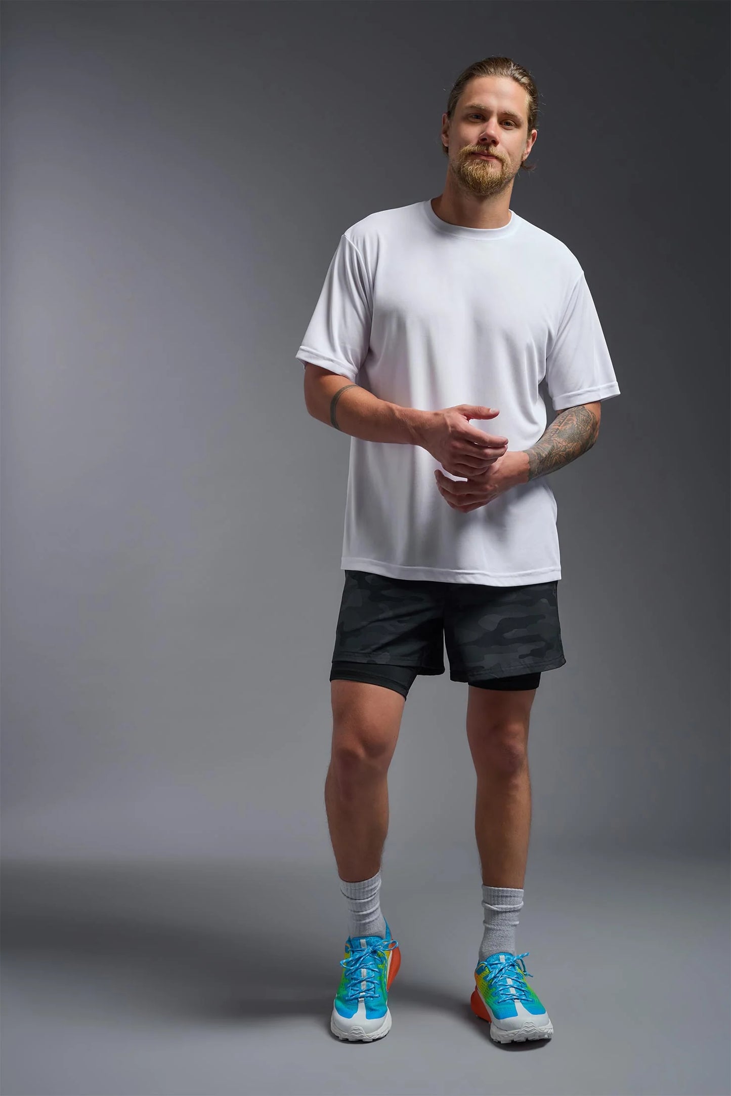 Man wearing a white t-shirt, black shorts, and colorful sneakers on a gray background