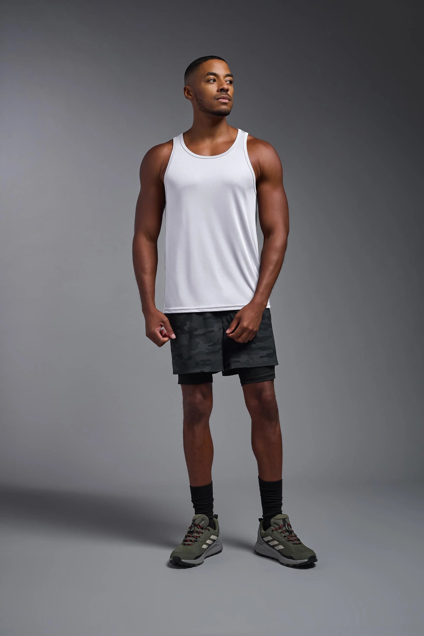 Man wearing a white tank top and black shorts on a gray background