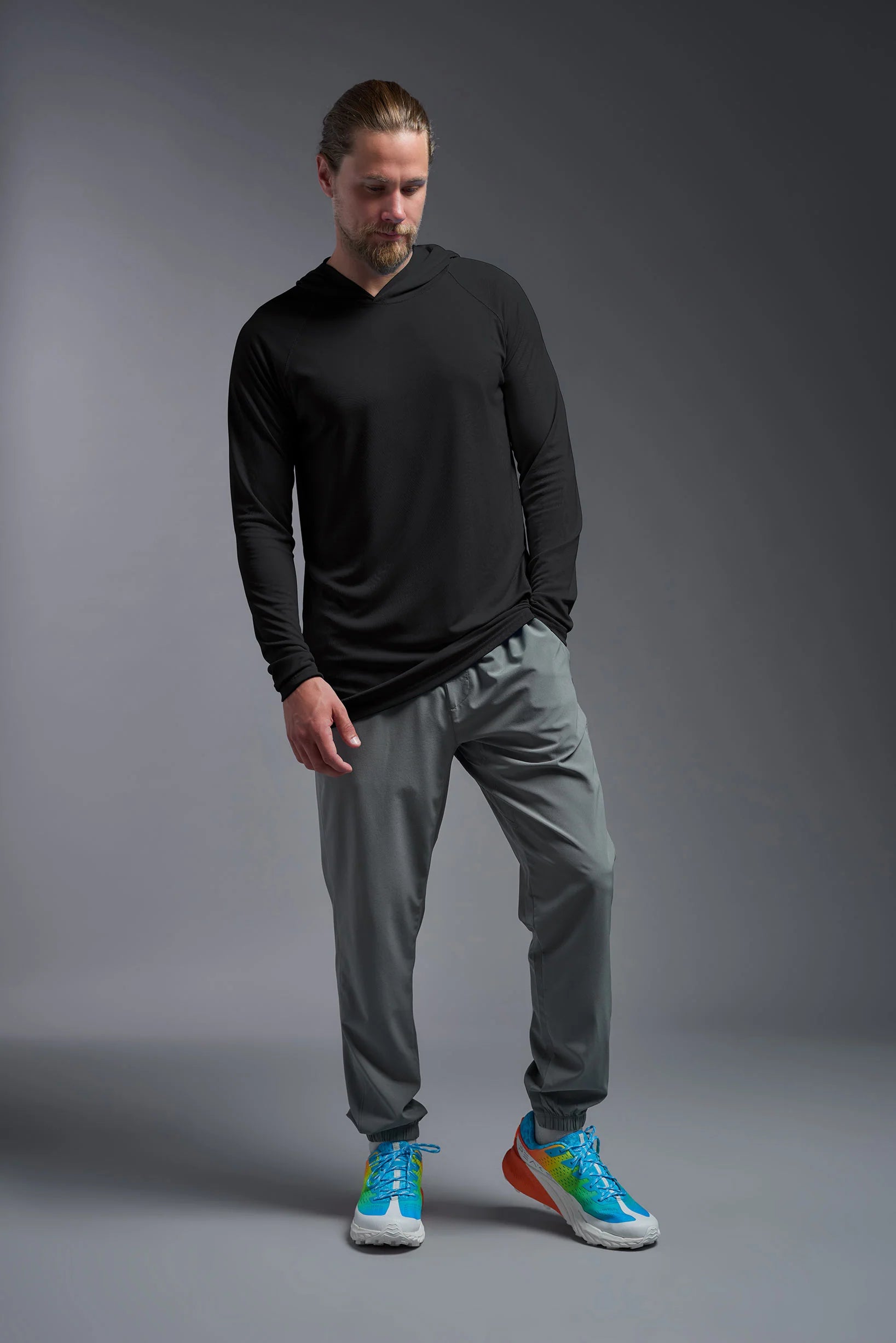 Man wearing a black long-sleeve shirt and gray pants with colorful sneakers on a gray background