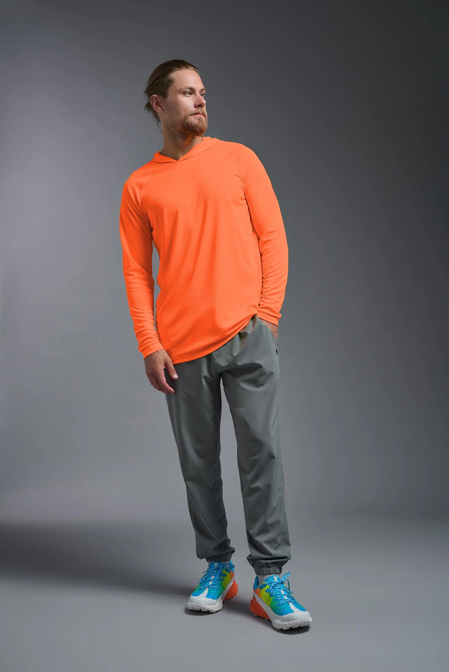 Man wearing an orange long-sleeve shirt and gray pants on a gray background