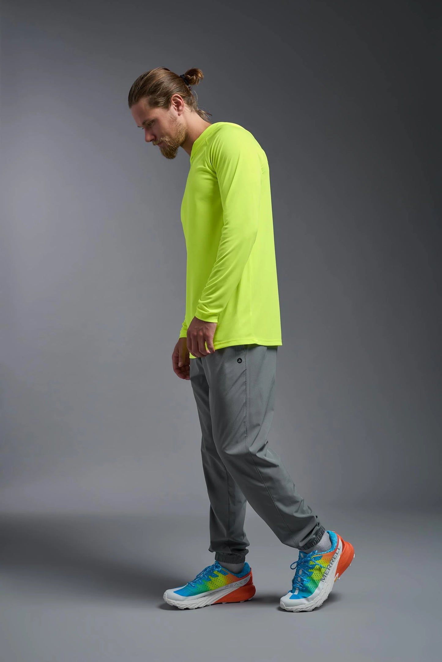 Man wearing a bright yellow long-sleeve shirt, gray pants, and colorful sneakers on a gray background