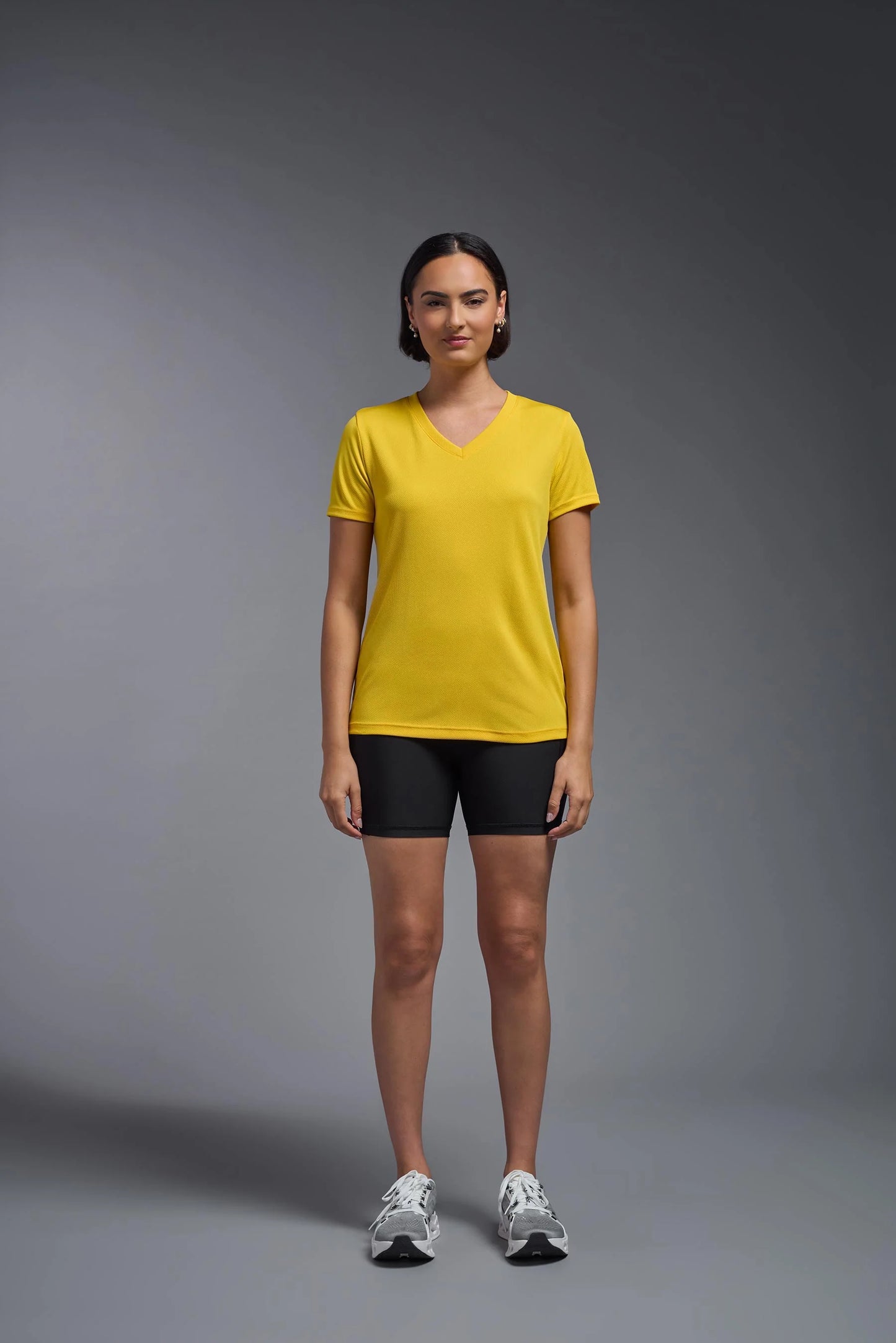 Woman wearing a yellow t-shirt and black shorts on a gray background