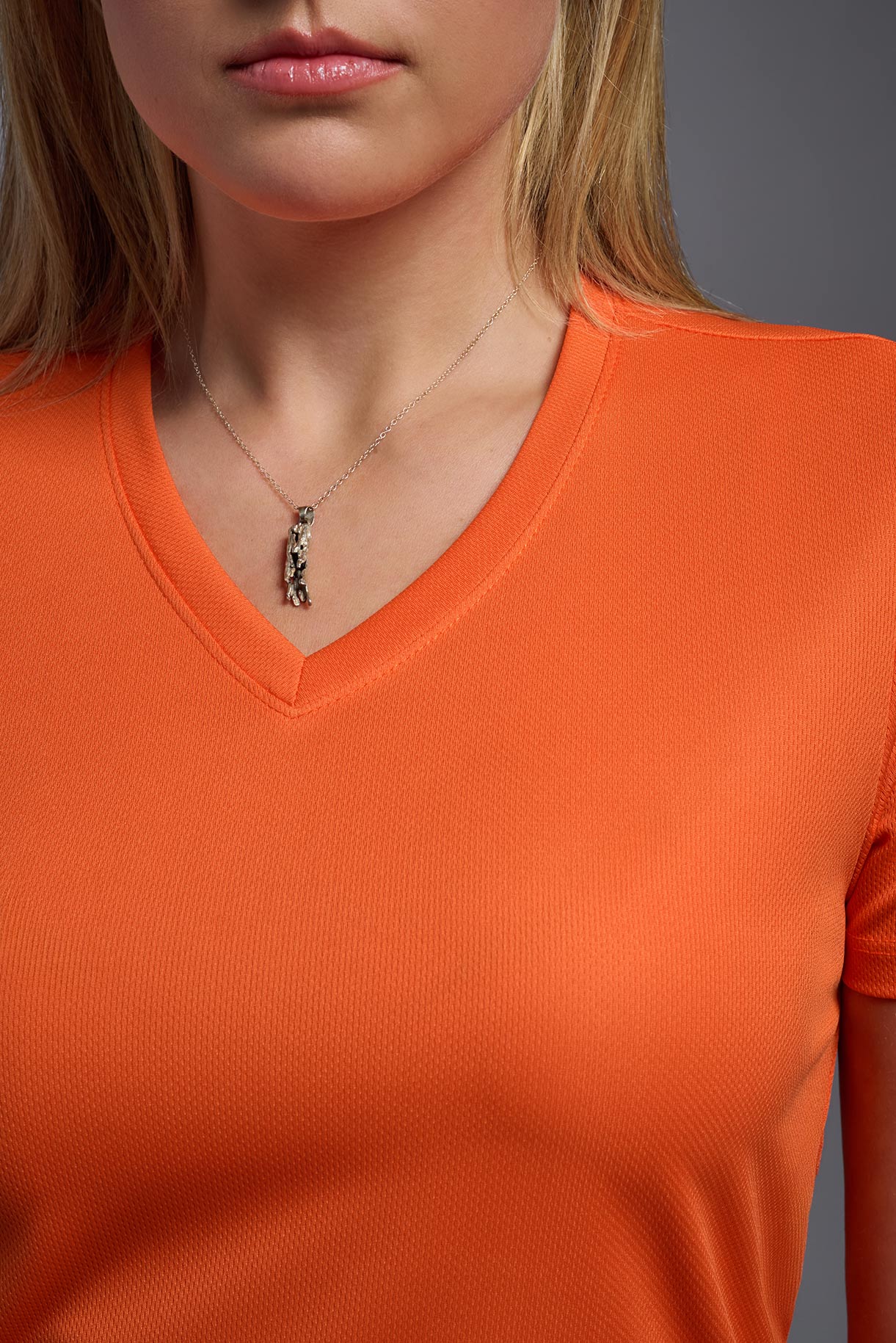 Person wearing an orange shirt with a necklace featuring a horse pendant.
