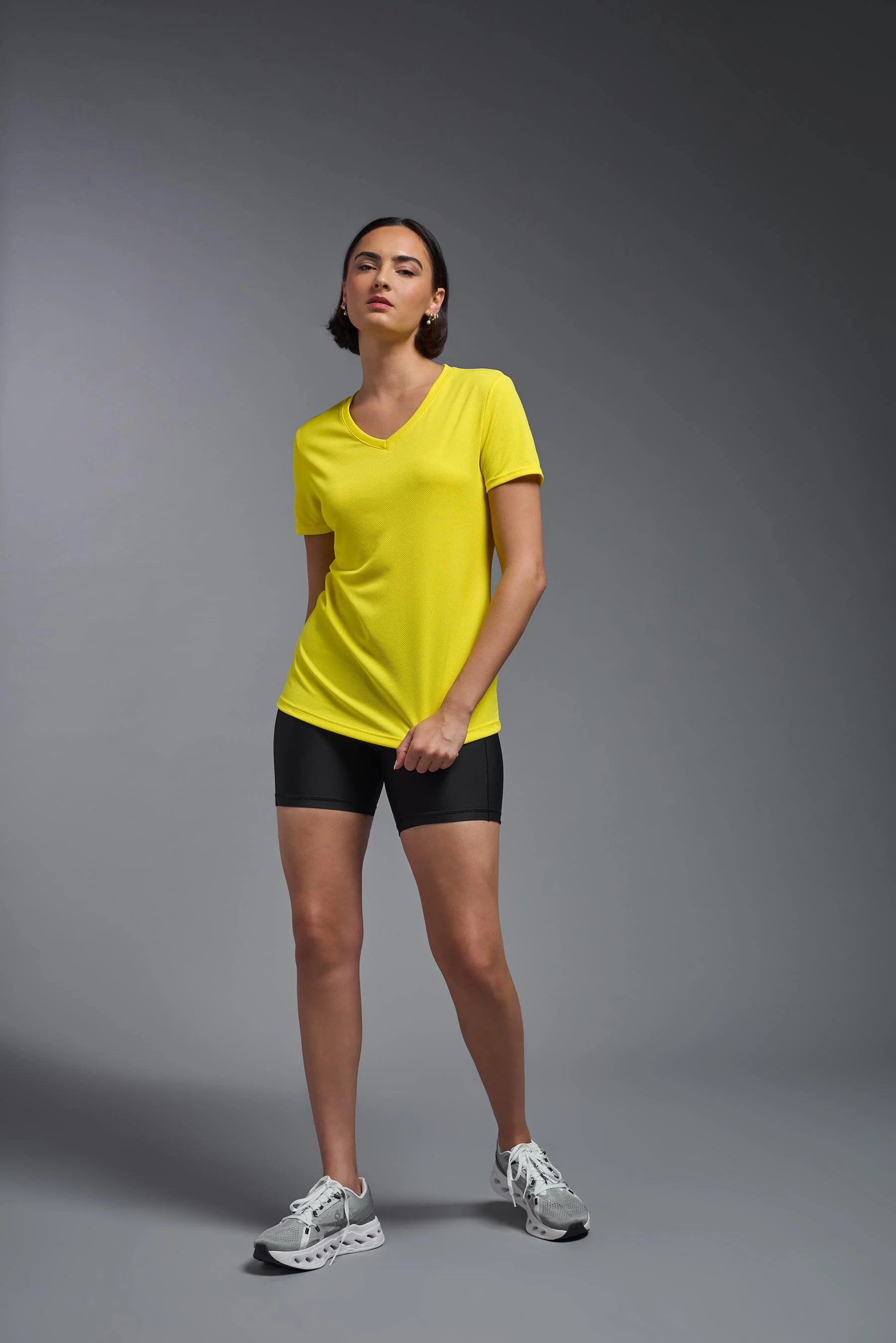 Woman wearing a yellow t-shirt and black shorts on a gray background