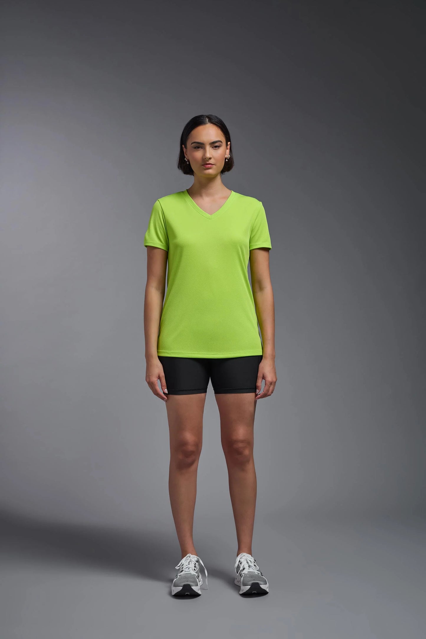 Person wearing a bright green t-shirt and black shorts on a gray background
