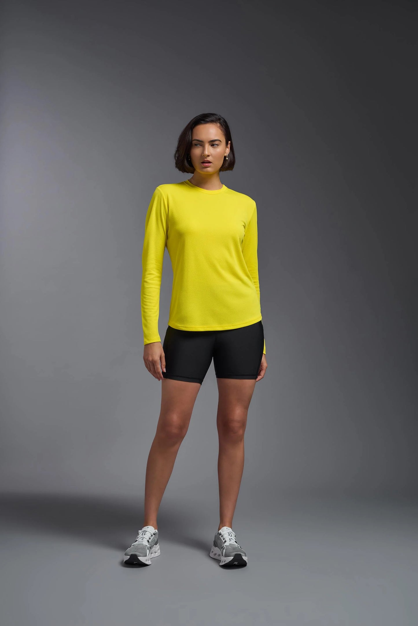 Person wearing a yellow long-sleeve shirt and black shorts on a gray background