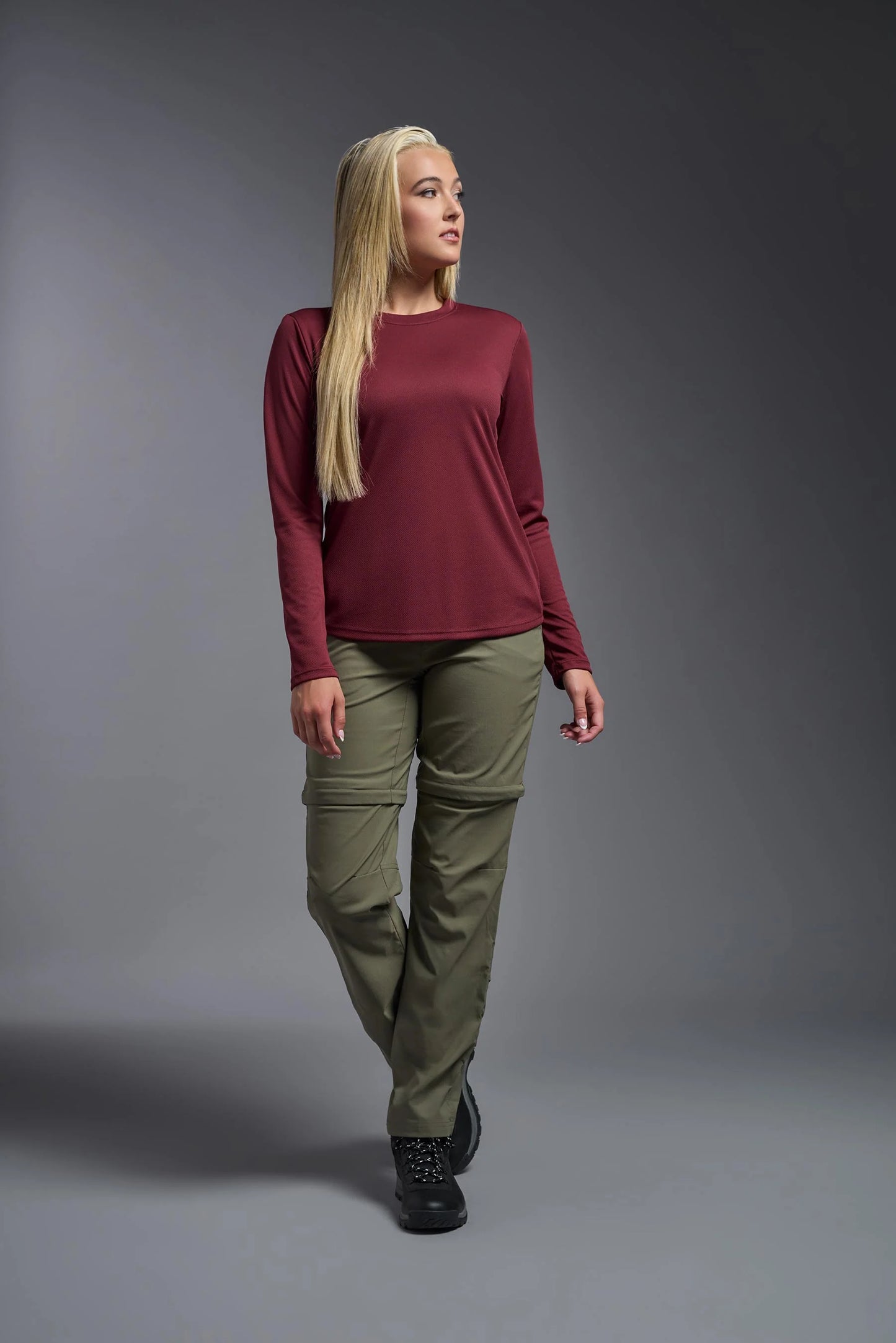 Woman wearing a burgundy long-sleeve top and green pants on a gray background